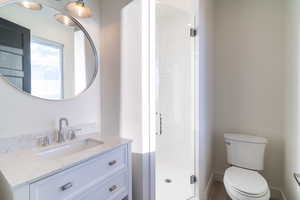 Bathroom featuring a shower with door, toilet, and vanity