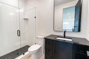 Bathroom featuring wood-type flooring, toilet, a shower with door, and vanity