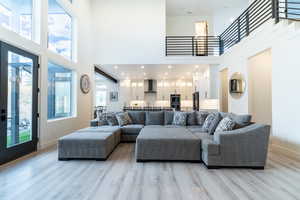 Spacious living room with grand lifted ceilings, light hardwood / wood-style floors, a healthy amount of sunlight, and a towering ceiling