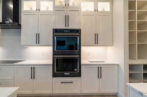 Kitchen with black appliances, wall chimney exhaust hood, and white cabinets