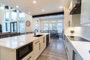 Kitchen may be my favorite place in the house! Kitchen with wall chimney exhaust hood, sink, a center island with sink, black appliances, and light wood-type flooring