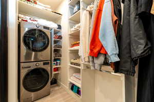 Clothes washing area with light hardwood / wood-style floors and stacked washer and clothes dryer