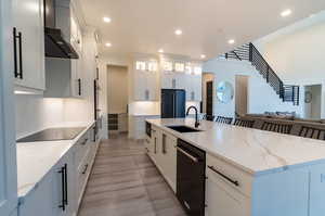 Kitchen with light hardwood / wood-style floors, sink, black appliances, wall chimney range hood, and white cabinets