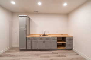 Add a fridge and you're set! Bar featuring sink, light hardwood / wood-style flooring, and gray cabinetry