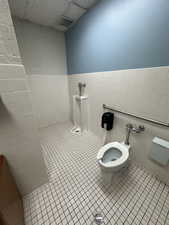 Bathroom featuring a drop ceiling, toilet, tile patterned floors, and tile walls