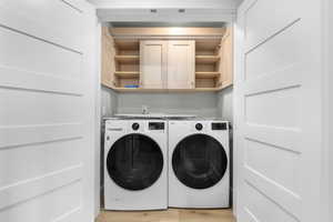 Laundry area with washing machine and dryer, light hardwood / wood-style flooring, and cabinets