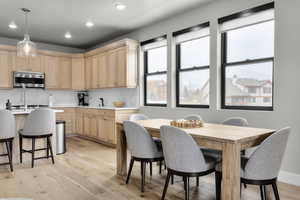 Kitchen with light wood-type flooring, light brown cabinetry, hanging light fixtures, and decorative backsplash