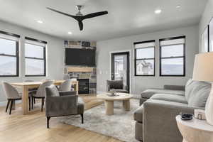 Living room featuring ceiling fan, light hardwood / wood-style floors, and a stone fireplace