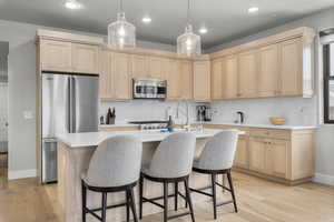 Kitchen featuring light brown cabinets, light hardwood / wood-style flooring, appliances with stainless steel finishes, and an island with sink