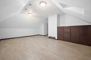 Bonus room featuring vaulted ceiling with skylight, light hardwood / wood-style flooring, and a textured ceiling