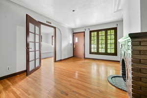 Unfurnished living room with a textured ceiling, light hardwood / wood-style flooring, french doors, and a brick fireplace