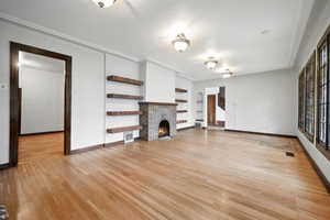 Unfurnished living room featuring built in shelves, light hardwood / wood-style flooring, and a brick fireplace