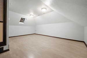 Additional living space with vaulted ceiling with skylight, light hardwood / wood-style flooring, and a textured ceiling