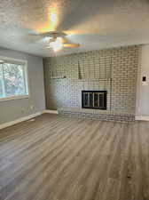 Unfurnished living room with wood-type flooring, brick wall, a textured ceiling, and a brick fireplace