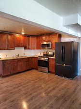 Kitchen with hardwood / wood-style flooring, sink, light stone countertops, appliances with stainless steel finishes, and a textured ceiling