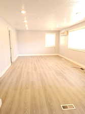 Empty room with a textured ceiling, light hardwood / wood-style flooring, and a wall mounted air conditioner