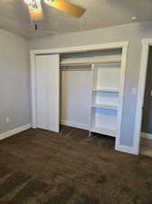 Unfurnished bedroom with ceiling fan, a closet, a textured ceiling, and dark colored carpet