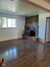 Unfurnished living room featuring a stone fireplace, dark wood-type flooring, a wood stove, and a textured ceiling