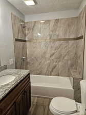 Full bathroom with toilet, tile patterned flooring, vanity, a textured ceiling, and tiled shower / bath combo