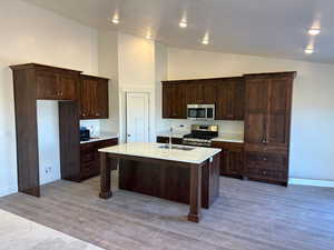 Kitchen with dark brown cabinetry, wood-type flooring, sink, a center island with sink, and stainless steel appliances