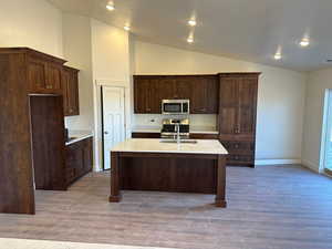 Kitchen with high vaulted ceiling, a kitchen island with sink, stove, and wood-type flooring