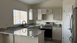 Kitchen with white cabinetry, sink, stainless steel appliances, and lofted ceiling