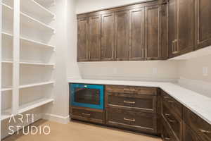 Interior space with light stone counters, dark brown cabinetry, and black microwave