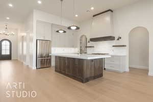 Kitchen featuring tasteful backsplash, premium range hood, an island with sink, pendant lighting, and high quality fridge