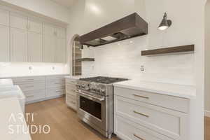 Kitchen featuring decorative light fixtures, high end stove, premium range hood, and tasteful backsplash