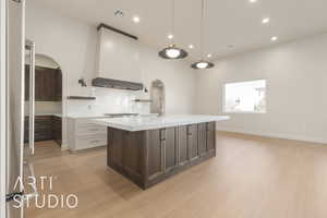 Kitchen featuring light wood-type flooring, dark brown cabinetry, white cabinetry, and wall chimney exhaust hood