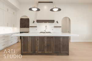 Kitchen featuring backsplash, an island with sink, white cabinets, and hanging light fixtures