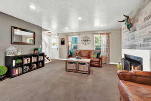 Living room featuring a textured ceiling, a large fireplace, and carpet flooring