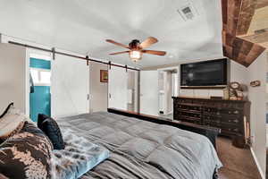 Carpeted bedroom featuring a barn door, a textured ceiling, and ceiling fan