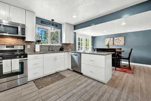 Kitchen featuring tile flooring, sink, stainless steel appliances, kitchen peninsula, and white cabinetry