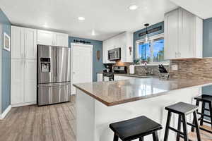 Kitchen with appliances with stainless steel finishes, pendant lighting, white cabinetry, and a textured ceiling