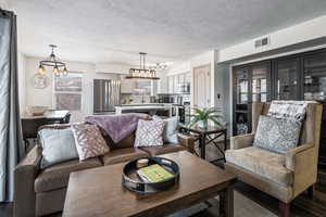 Living room with rail lighting, an inviting chandelier, dark wood-type flooring, and a textured ceiling