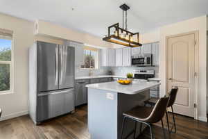 Kitchen featuring a center island, decorative light fixtures, appliances with stainless steel finishes, dark wood-type flooring, and tasteful backsplash