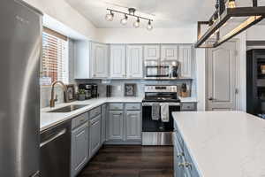 Kitchen with stainless steel appliances, decorative backsplash, sink, light stone countertops, and dark hardwood / wood-style flooring