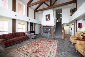 Living room featuring a fireplace, high vaulted ceiling, beamed ceiling, and dark tile patterned flooring