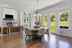 Dining room featuring dark hardwood / wood-style floors, a chandelier, a stone fireplace, french doors, and crown molding