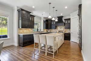 Kitchen featuring premium range hood, decorative backsplash, an island with sink, and a kitchen bar