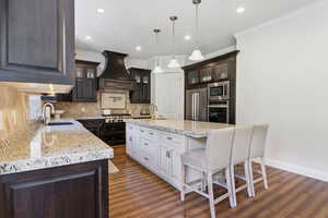 Kitchen with custom exhaust hood, a kitchen island with sink, appliances with stainless steel finishes, and dark hardwood / wood-style floors