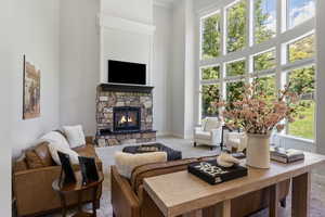 Living room featuring a wealth of natural light, carpet floors, a towering ceiling, and a stone fireplace