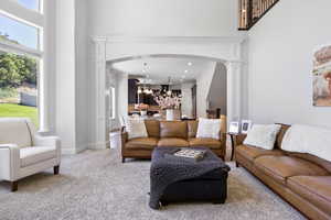 Living room featuring light colored carpet, ornamental molding, a towering ceiling, decorative columns, and an inviting chandelier