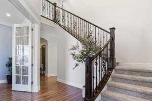 Staircase with a towering ceiling, crown molding, hardwood / wood-style floors, and ornate columns