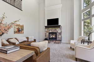 Living room with carpet, a stone fireplace, and a towering ceiling