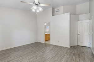 Unfurnished bedroom featuring ceiling fan, ensuite bathroom, light hardwood / wood-style floors, and a high ceiling