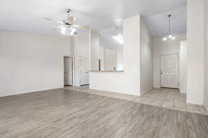 Unfurnished living room with ceiling fan with notable chandelier, high vaulted ceiling, and light hardwood / wood-style floors