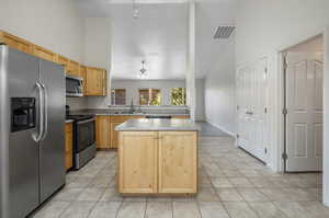 Kitchen featuring a center island, high vaulted ceiling, light brown cabinetry, ceiling fan, and stainless steel appliances