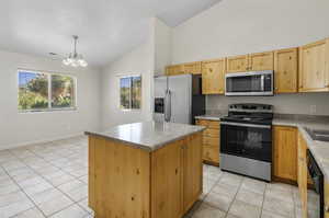 Kitchen featuring stainless steel appliances, decorative light fixtures, a chandelier, a kitchen island, and light tile patterned flooring